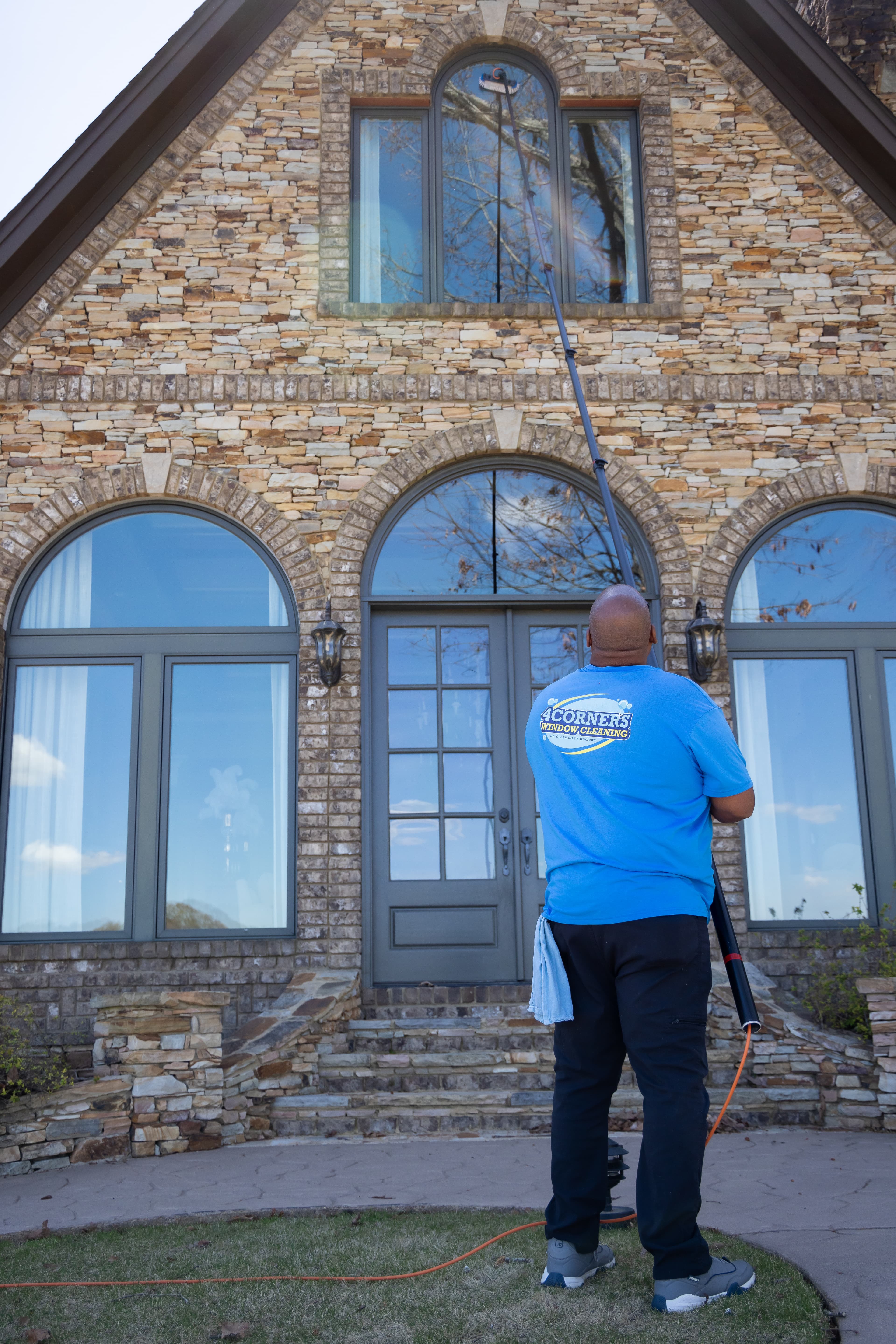 Window cleaner using a long extension pole to wash high windows of a stone house.